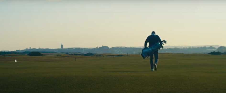 Rear view of caddy walking with golf clubs