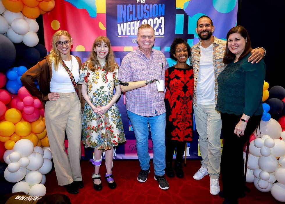 Six people posed, arms around each other. Balloons and "Inclusion Week 2023" behind them.