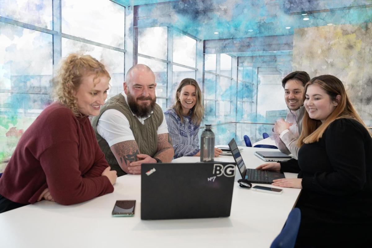 A group of seated people smiling at a laptop on a conference table.