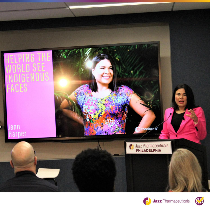 A speaker at a podium. A display "Helping the world see indigenous faces" .