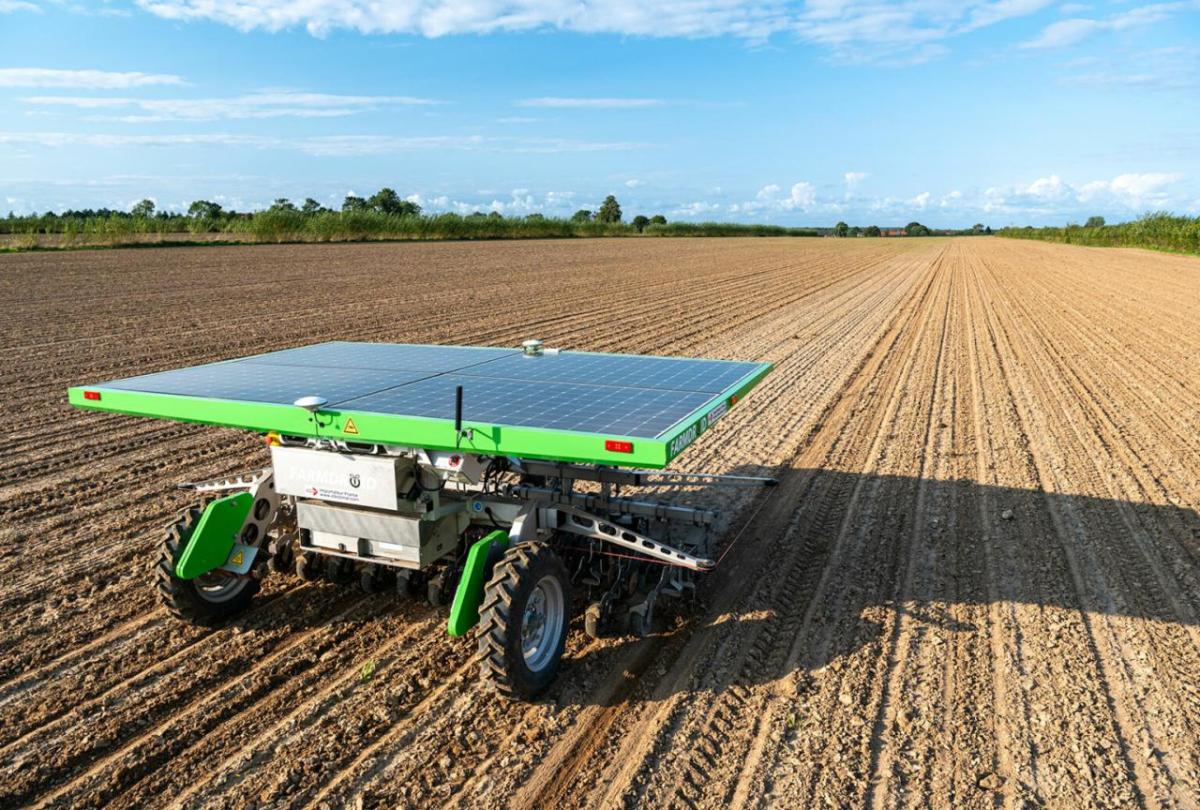 A solar panel on top of a small farm implement in a bare field. 