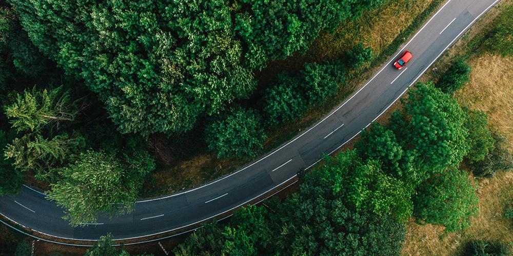 Aerial view of a single red car on a two-way road through forested area