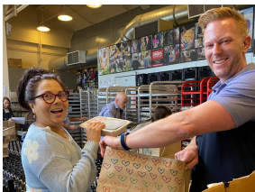 Two people smiling holding a bag in a bakery.