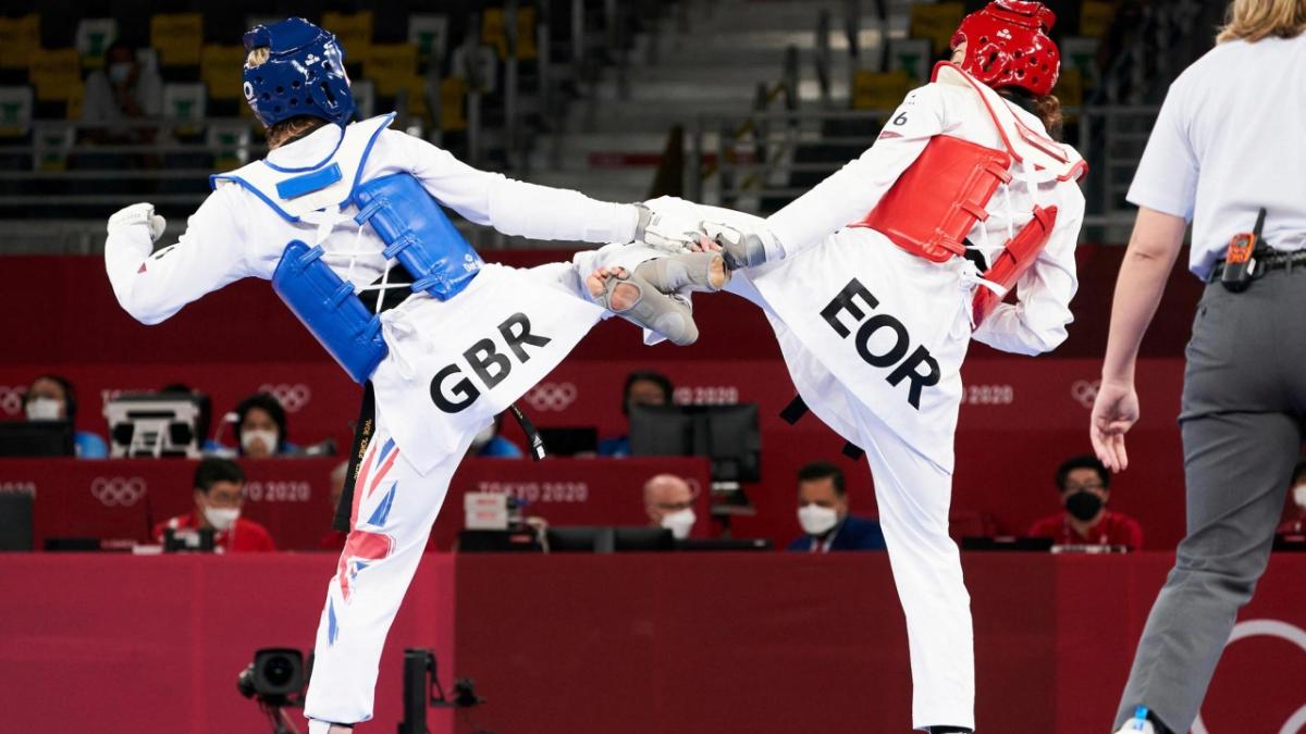 two people in a fighting match, wearing protective gear, in a stadium