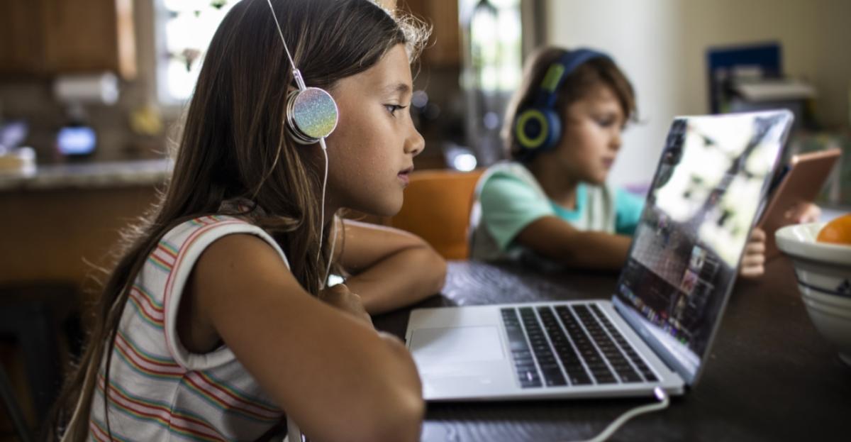 two kids wearing headphones, each on a laptop in a kitchen setting