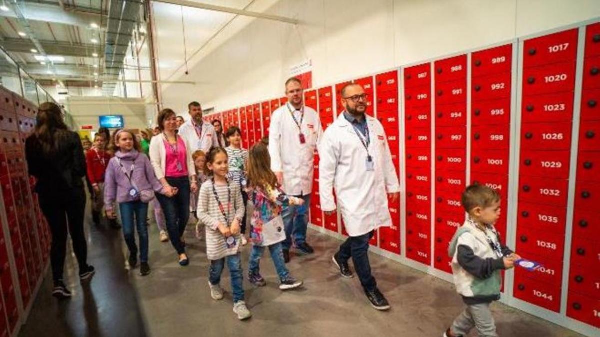 Adults and children walking down a hall lined with red boxes.