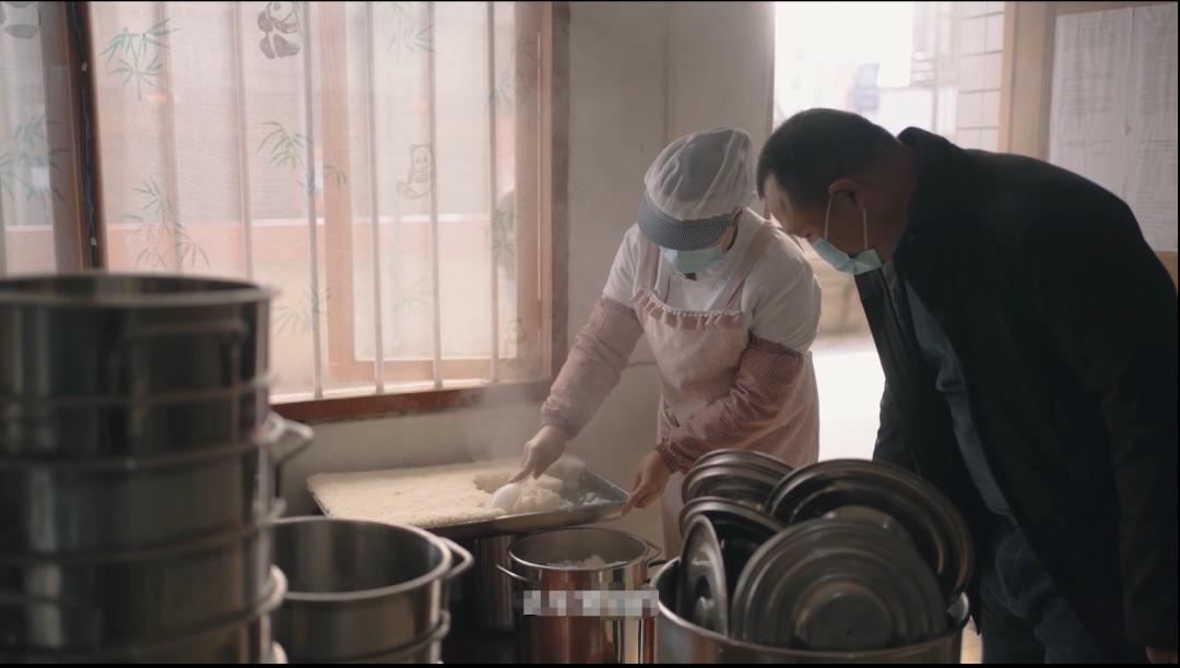 One person scooping rice into a bowl as another watches.