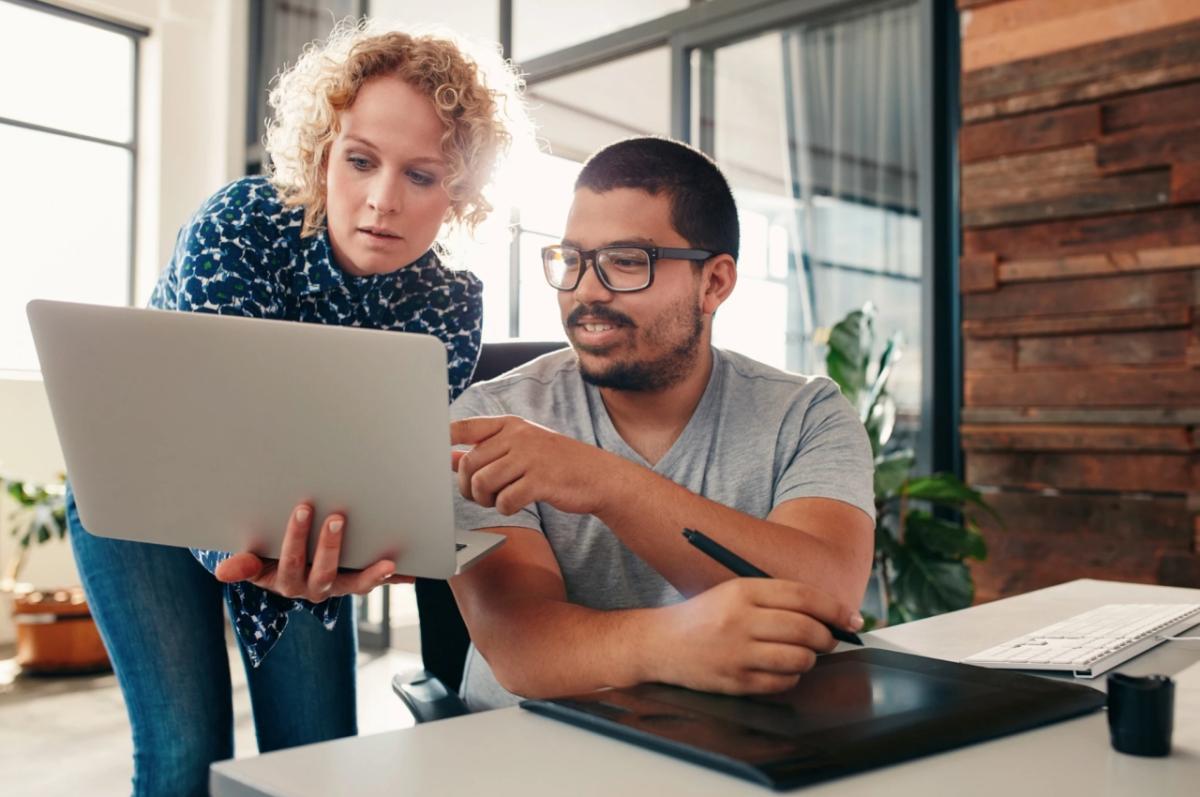 Two people looking at the same laptop in an office setting