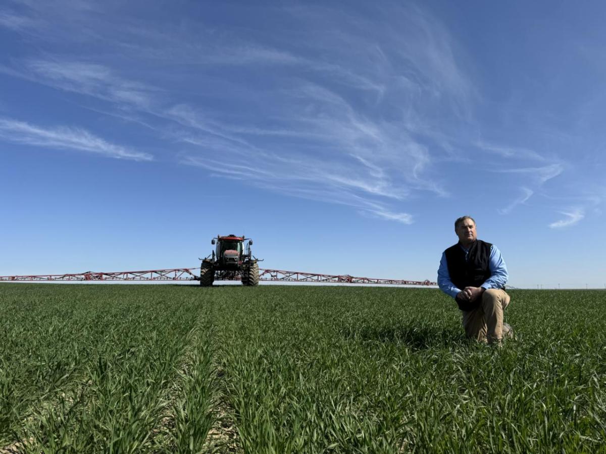 A person on one knee in a field with a machine in the background