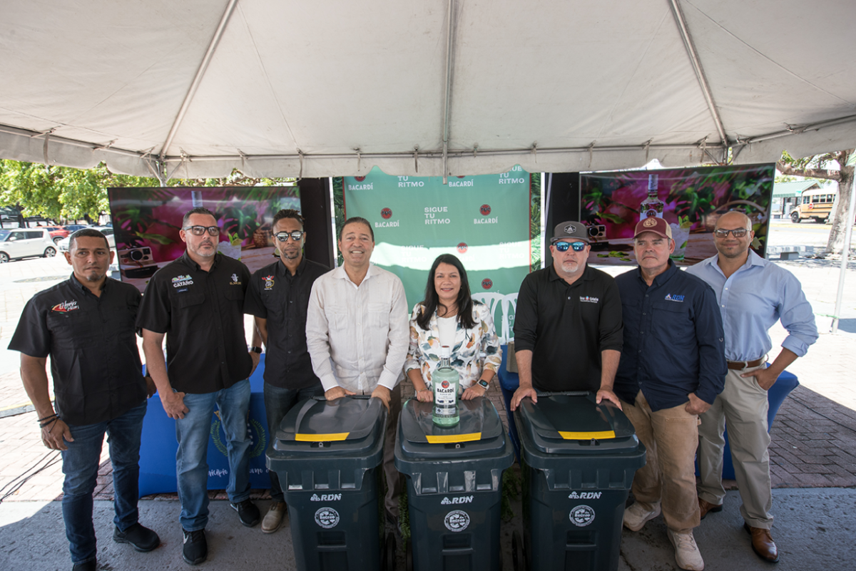 8 people standing together under a tent with 3 recycling bins