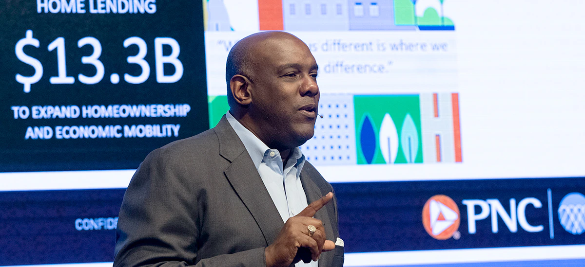 A person speaking with a large display behind them with PNC logo and "Home lending $13.3 B to expand homeownership and economic mobility" visible