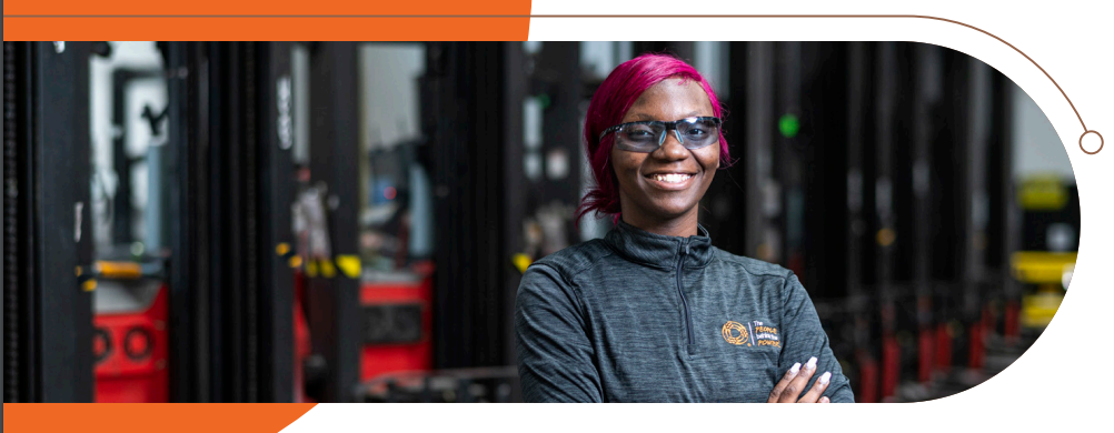 A smiling person with arms crossed in front of a row of machines.