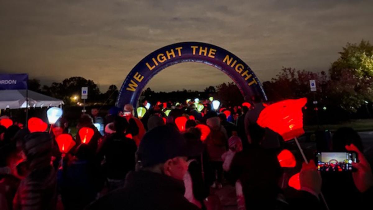 "We light the night" banner, red lanterns held by a group of participants at a nighttime event.