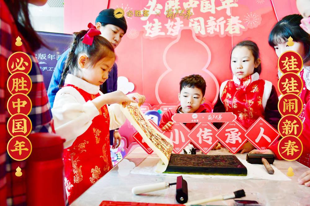 children watch as one lifts a piece of paper off an ink block. Signs in Chinese behind them and to the sides.