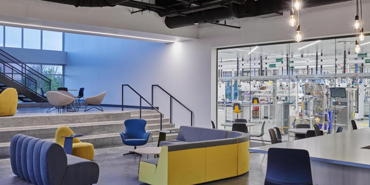 A lobby with blue and yellow seats, which also has a large window looking into a lab