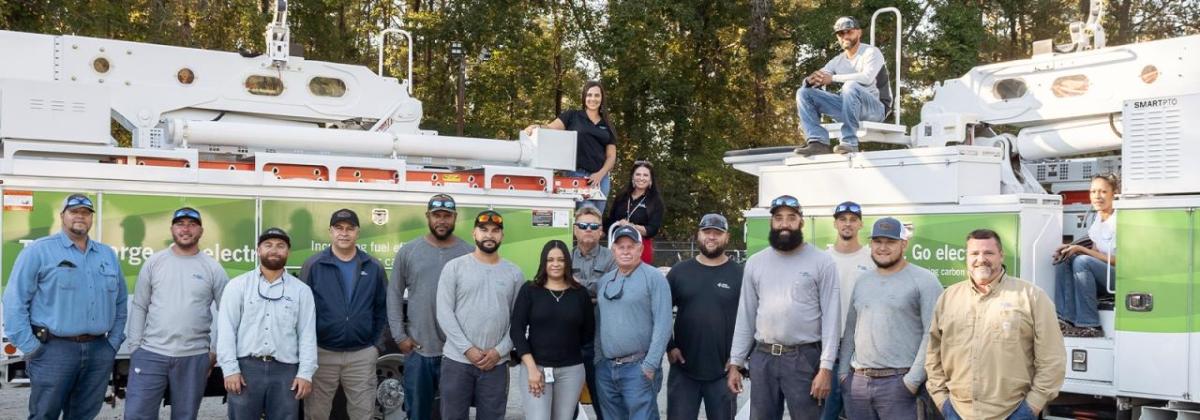 A large group of employees posed in front of two large trucks with extension buckets.