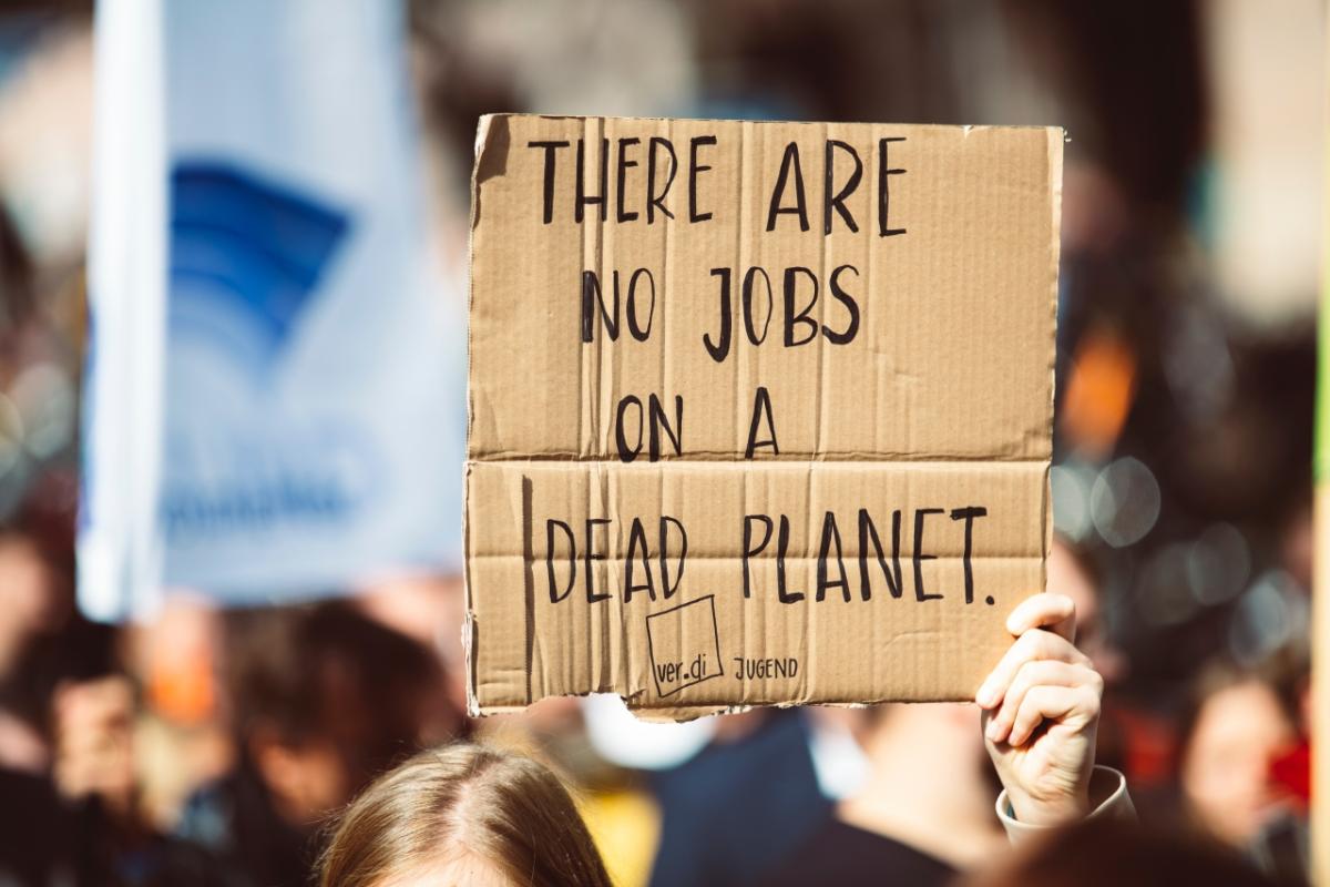 Protester with a cardboard sign reading "THERE ARE NO JOBS ON A DEAD PLANET"