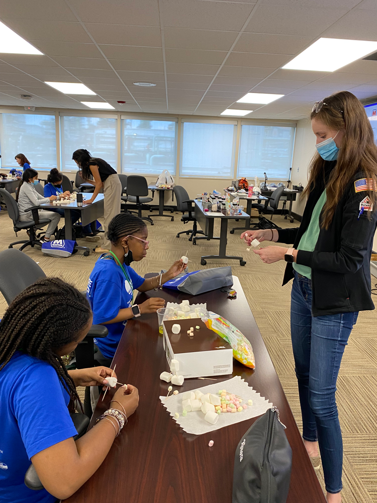 an adult works with two students at a desk to make marshmallow molecules