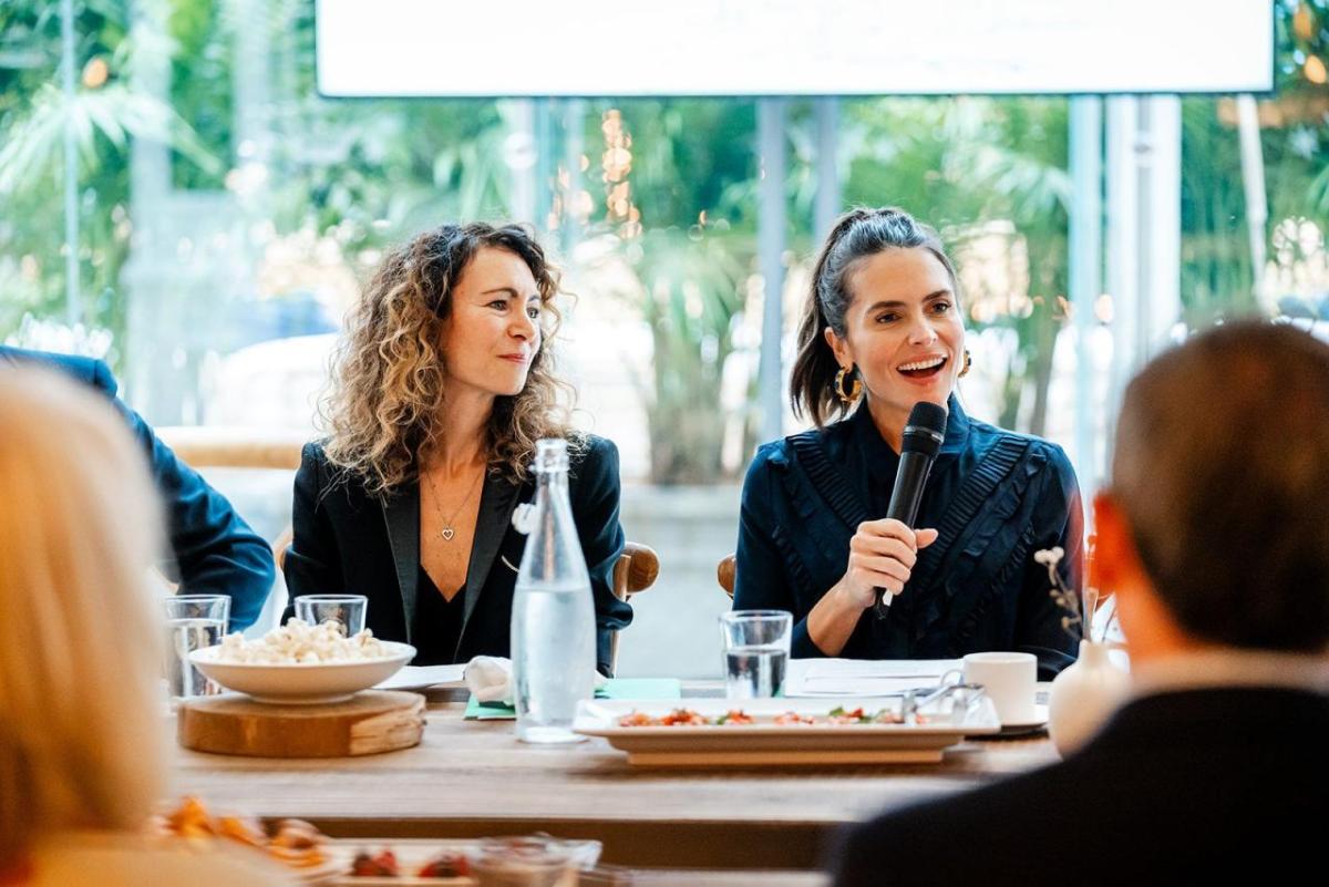 People seated at a dining table. One speaking with a microphone.