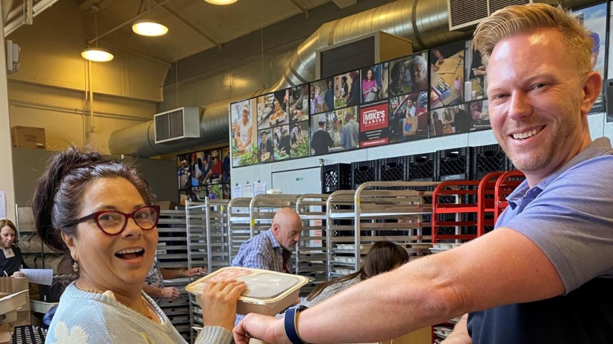 two people packing meals, many tray carts behind them