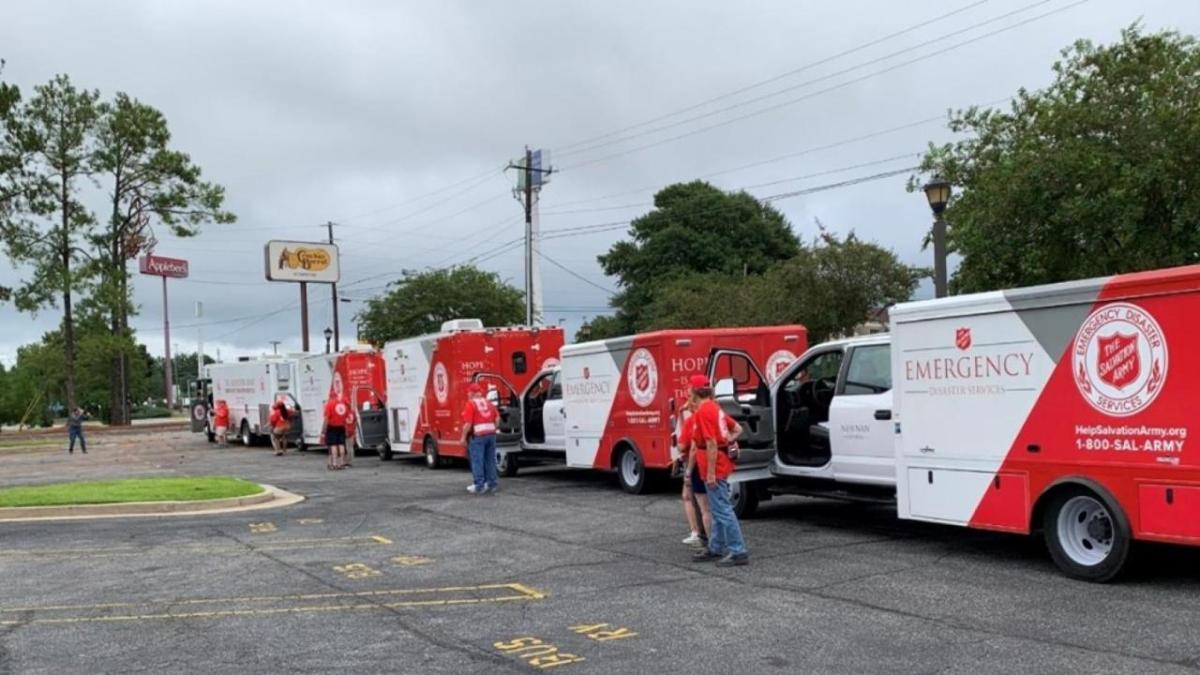 A row of parked box trucks in a parking lot, a person standing by each driver side door.