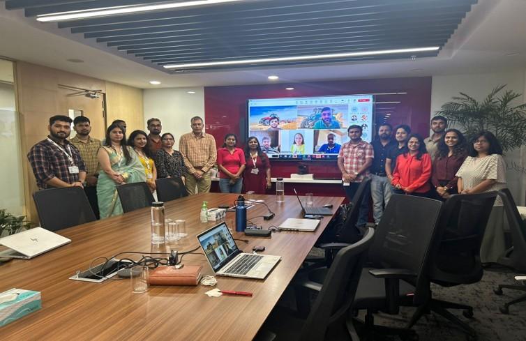 A group of people smiling and standing together in a board room in front of a large screen