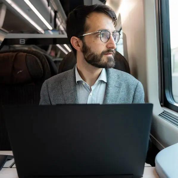 Ruggero Rollini looking out a train window, laptop open.