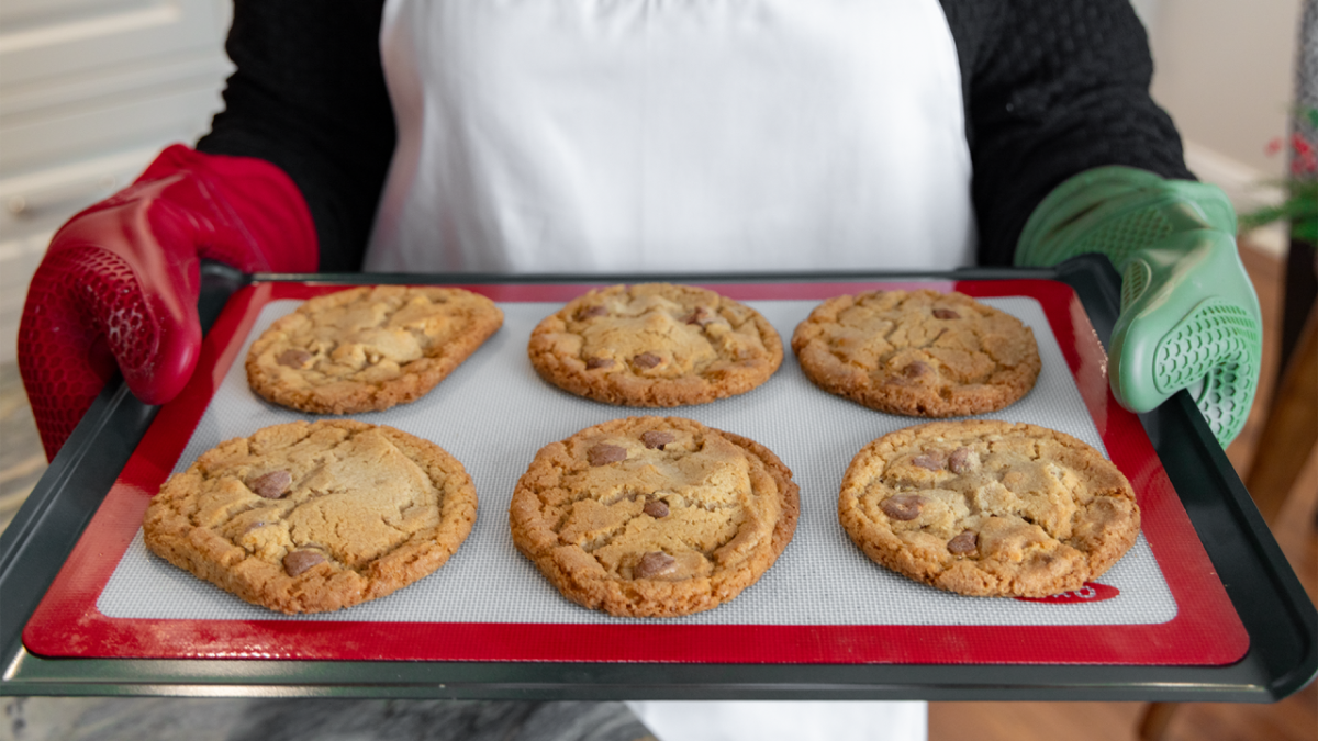 Donna Kelce holds a tray of cookies. She has a red and green oven mitt on each hand.