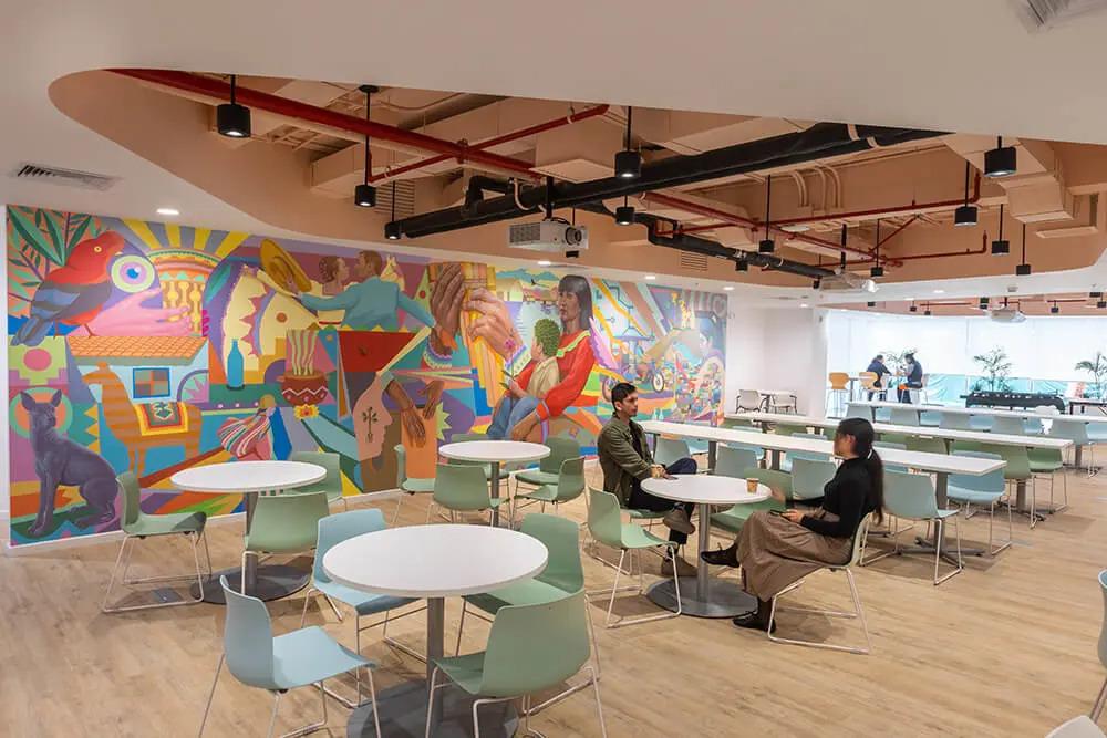 Two people at a circular table in a cafeteria type setting, a colorful mural on one wall.