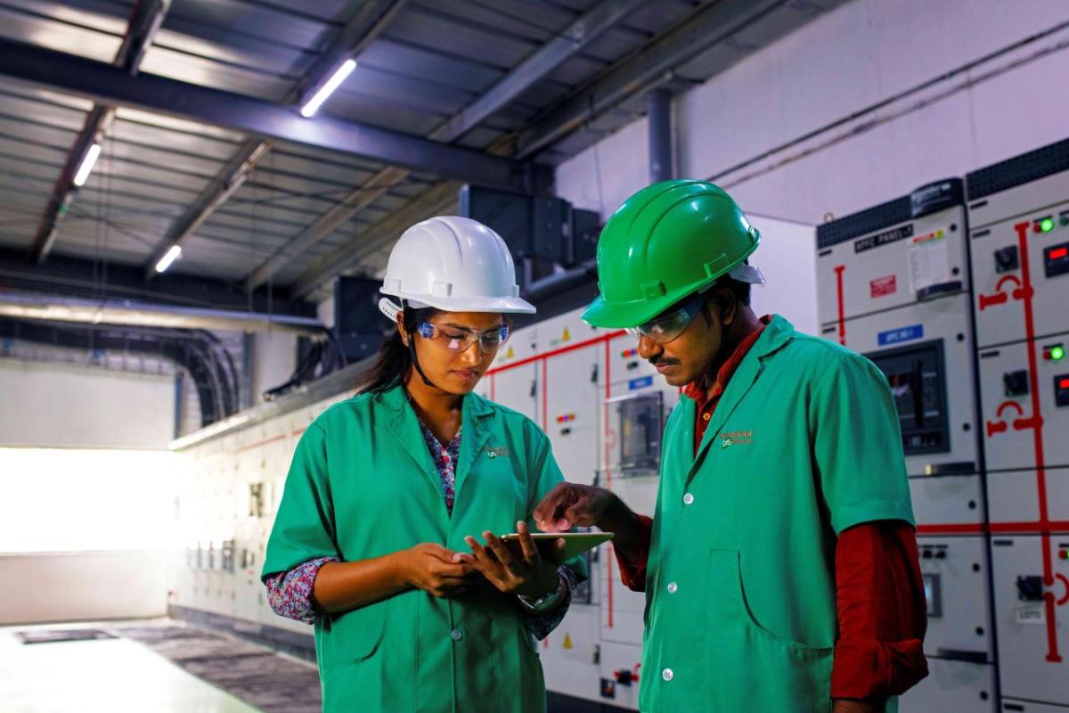 Two people in uniforms and hard hats, one pointing at a tablet being held by the other.