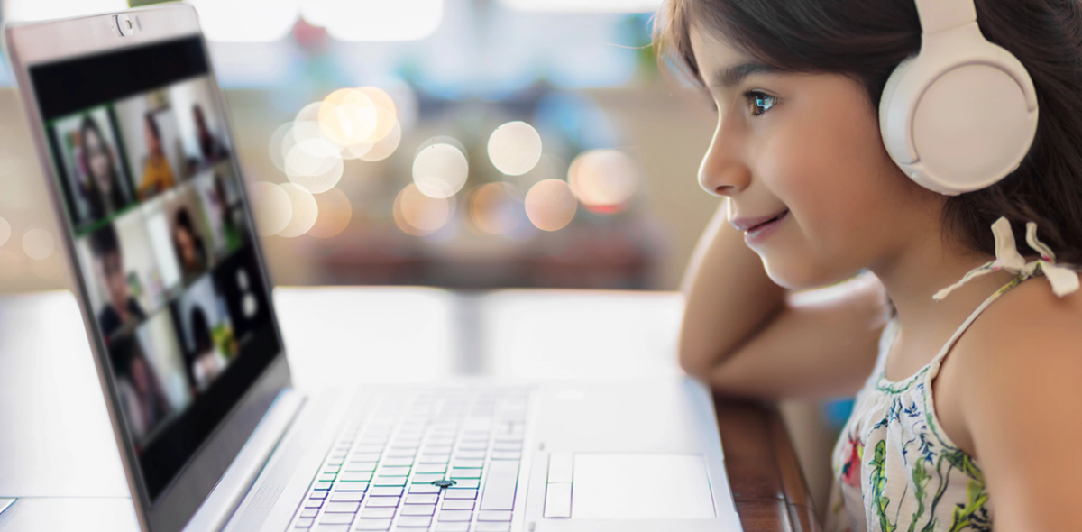 smiling child wearing headphones while looking at a laptop screen