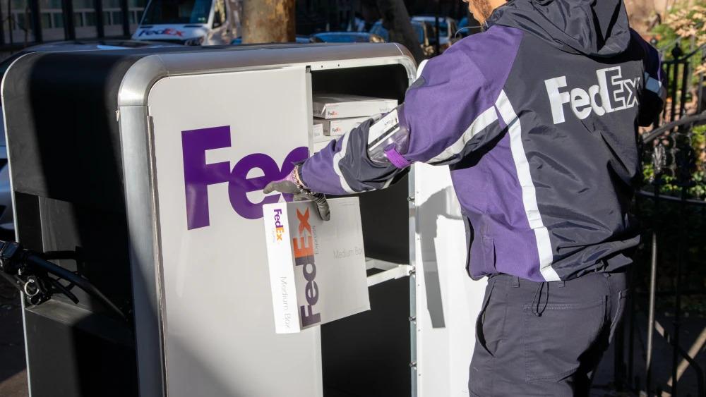 A person in FedEx uniform opening a tall cart with FedEx Express logo on it and pulling out a package.