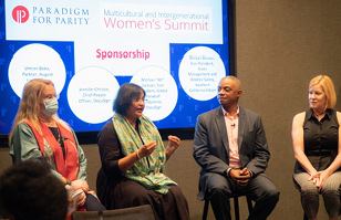 A four person panel, one speaking. A digital screen "Paradigm for Parity" showing.