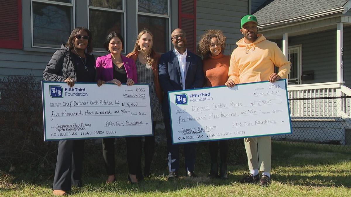 People standing in front of house holding oversized checks