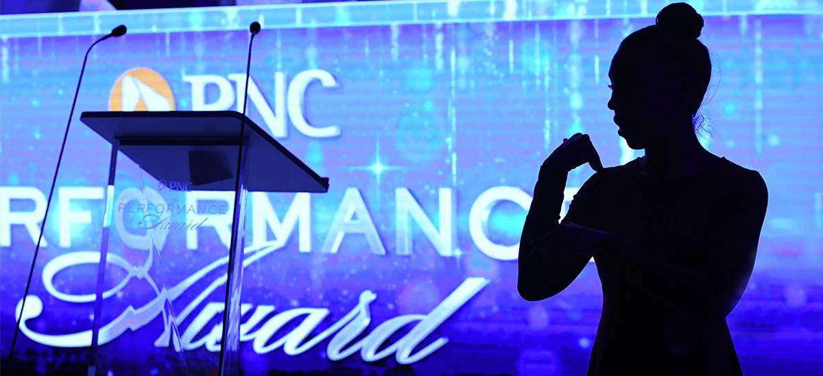"PNC Performance Awards" projected on a large screen behind a podium. A person in shadow beside it.