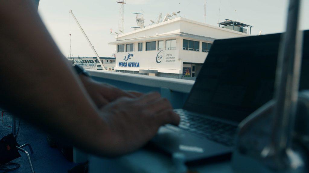 A person working at a laptop, a fishing boat outside their window.