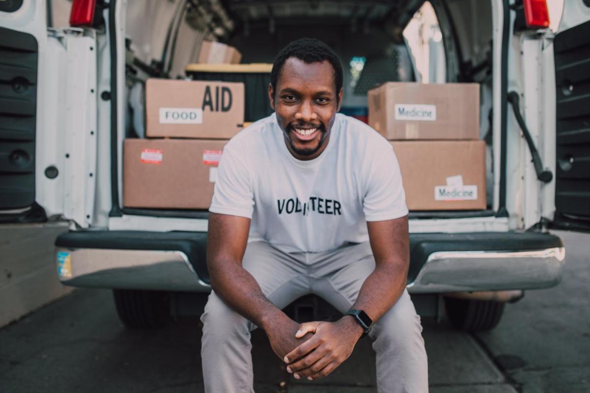Volunteer man sitting in the open bay of a van filled with boxes and supplies.