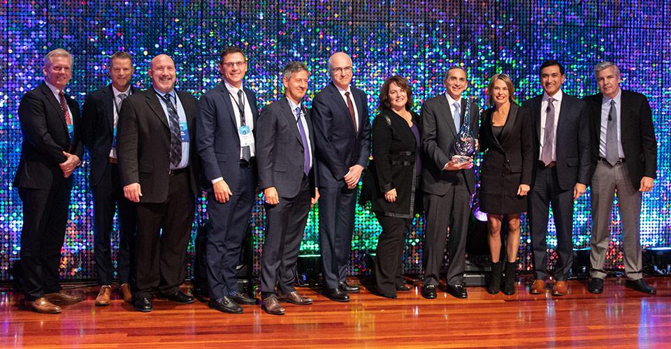 Group of people in a row on a stage. One holding an award.