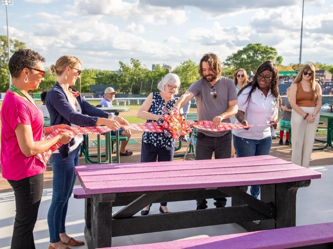 a group of people cut a ribbon over a picnic table outside