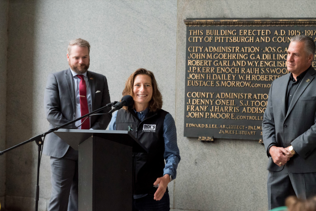 Spokesperson at a podium, two others behind them