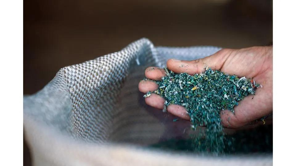 Creating a renewable plastics supply chain. Image courtesy of BRASKEM A person holding shredded plastic above a bag.