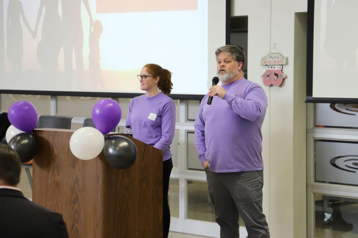 Two people in matching purple shirts behind a podium.