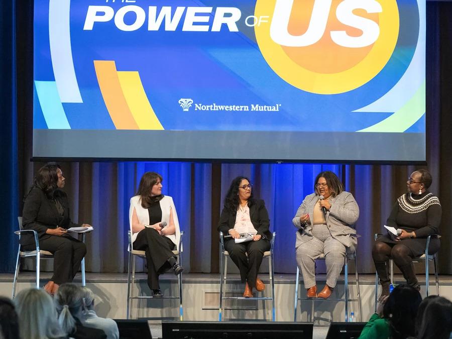 Five people with microphones seated on a stage in front of an audience.
