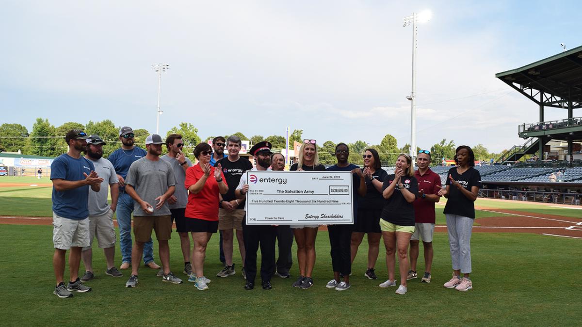 A group of people on a baseball field, some holding a large check.