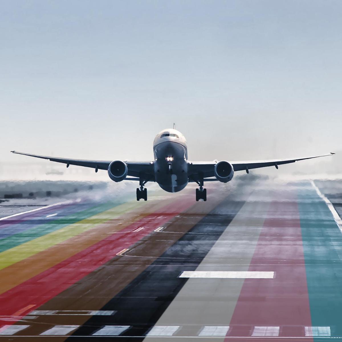 An airplane landing on a runway colored with LGBTQ+ flag colors
