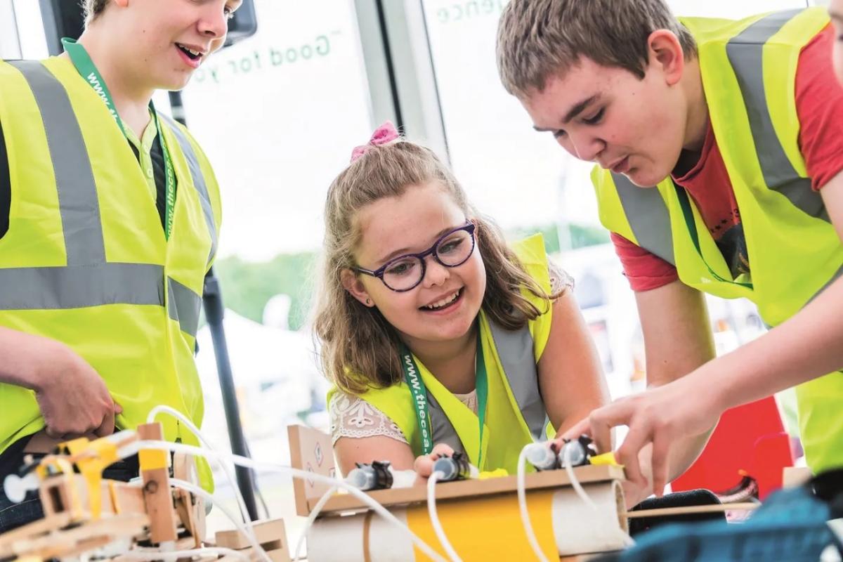 three children in high visibility vests work on an engineering project in a classroom