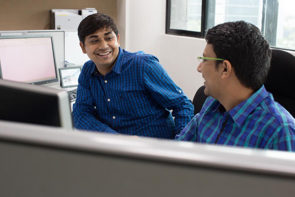 Two men speaking while seated in a cubicle.