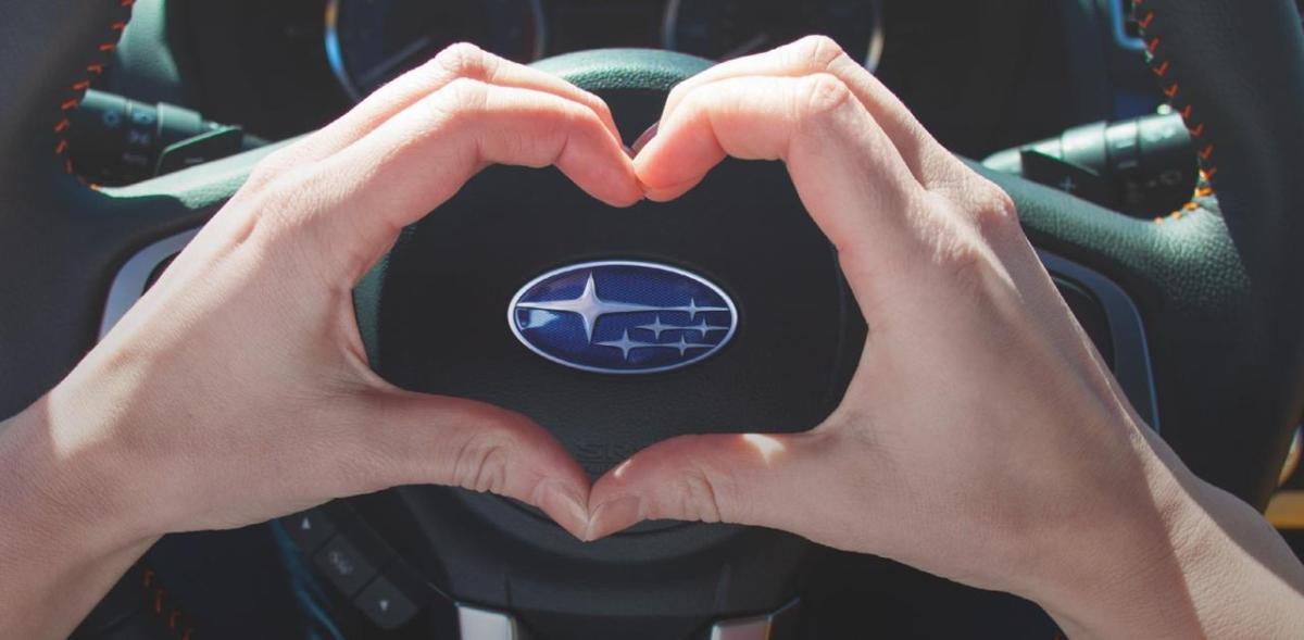 Forbes recognizes Subaru as one of the “Best Brands for Social Impact” in inaugural list based on consumer survey. heart hands being made over Subaru steering wheel