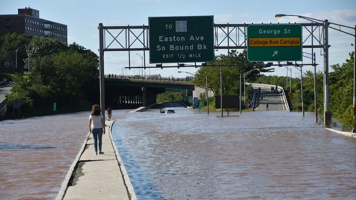 Flooded motorway. Two pedestrians on walkway with street flooded on either side.