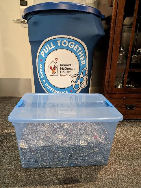 A blue barrel with a label "Pull Together" behind a clear tub full of soda can pull tabs.